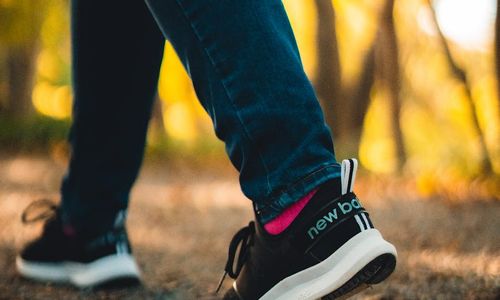 Close-up of feet walking on a path covered with autumn leaves.